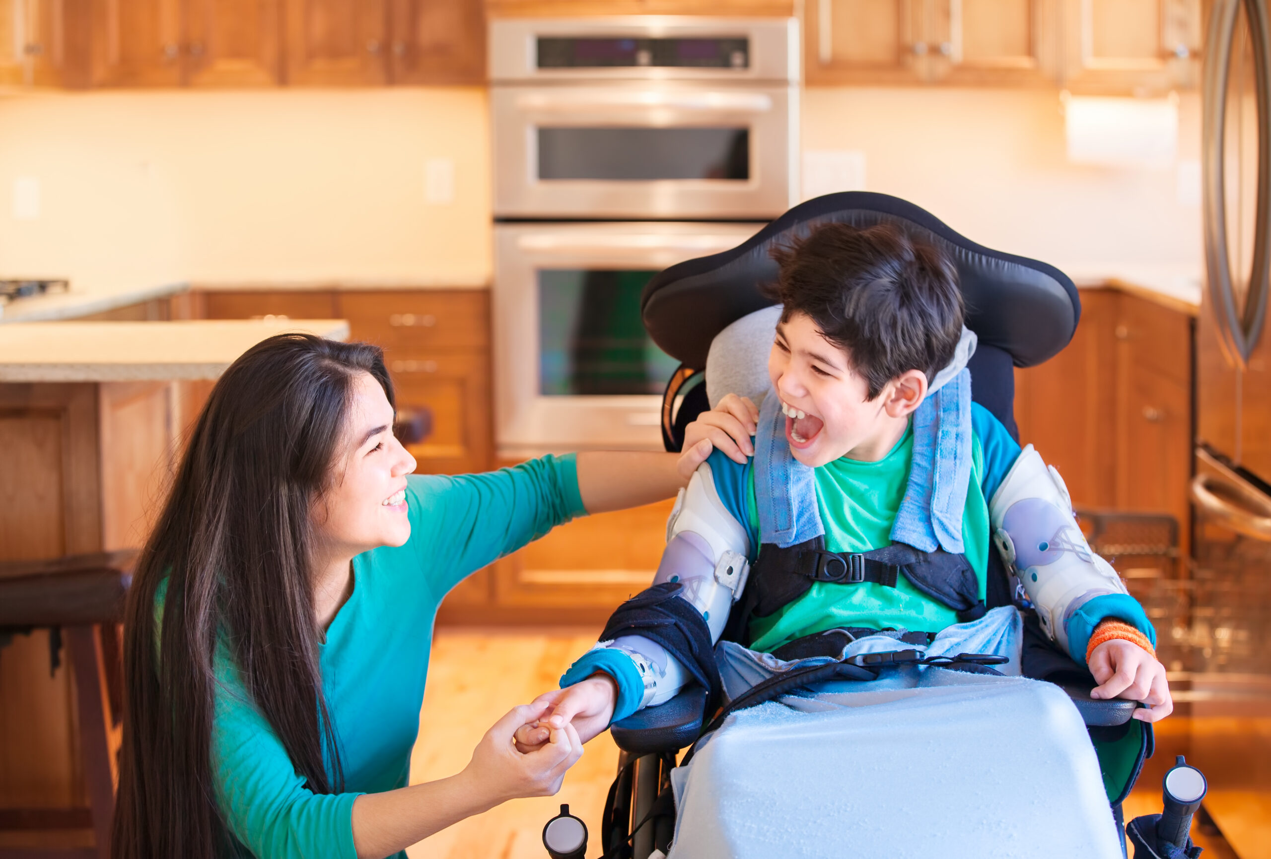 Nine year old disabled boy in wheelchair laughing with teen sister in kitchen