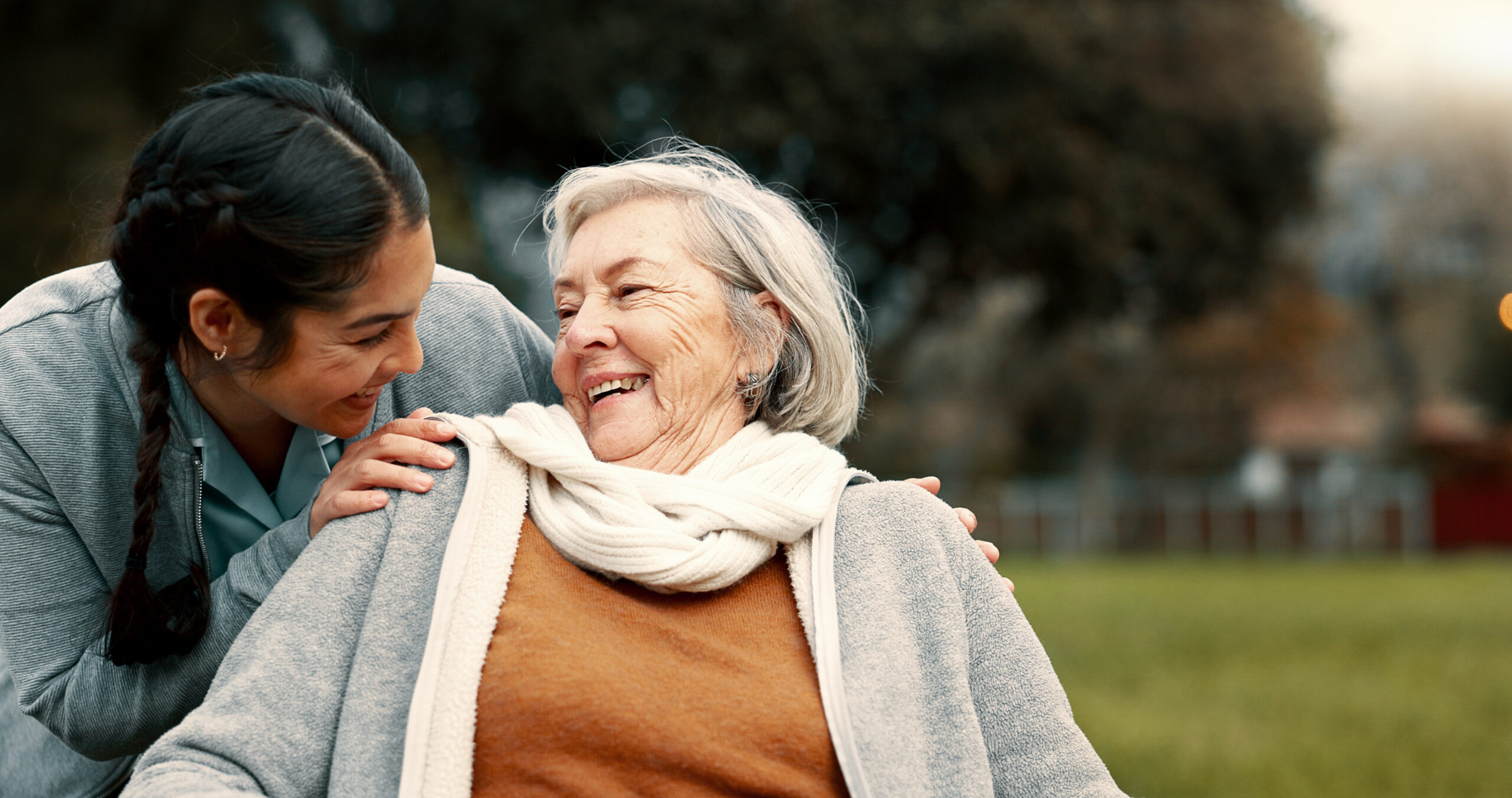 Caregiver helping woman with disability in park for support as the two laugh in conversation.